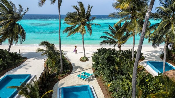 Un resort en la playa con piscina, palmeras y vista al océano.