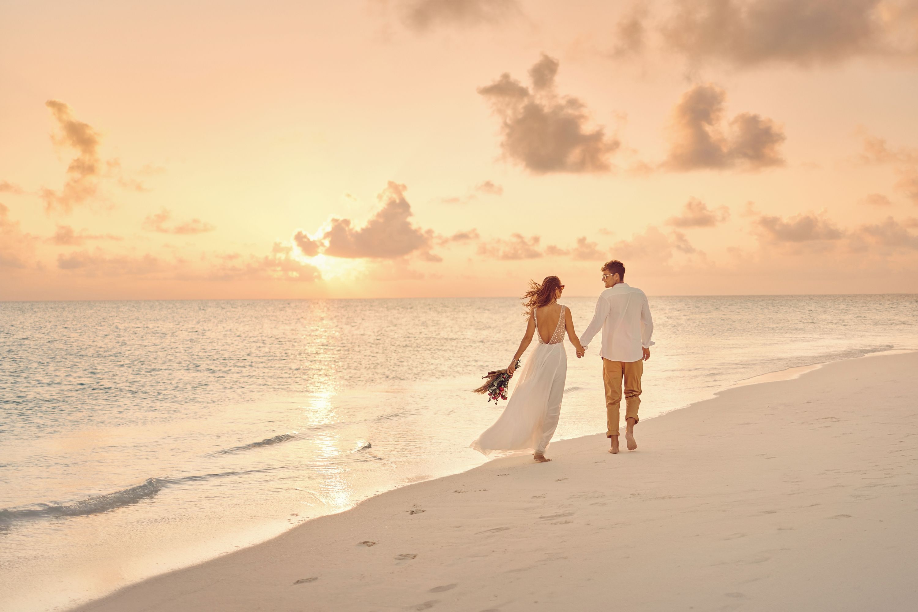 A couple walking on a beach at sunset.