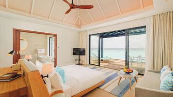 A bedroom with a bed, a desk, a TV, and a balcony with a view of the sea.