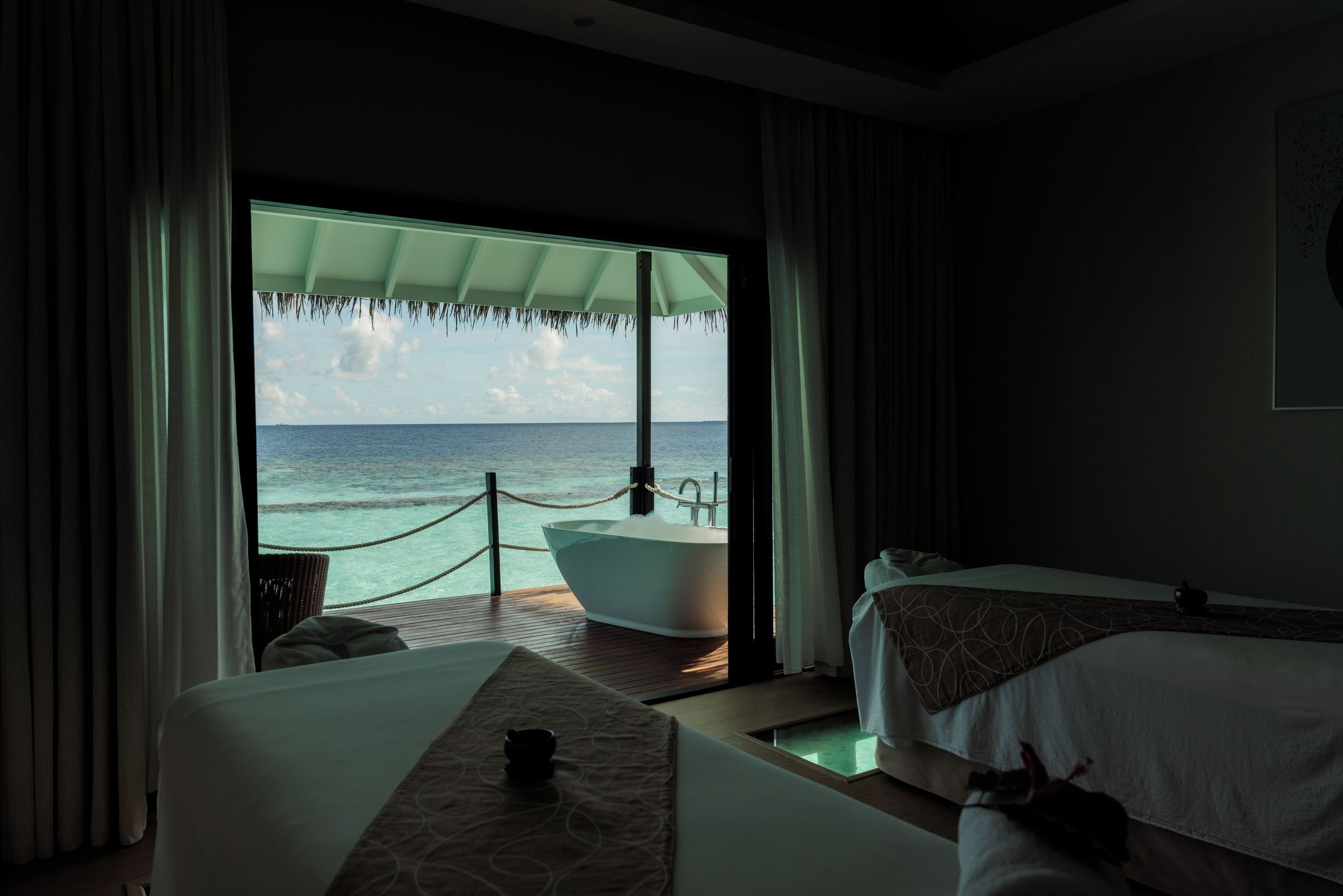 A room with a large window, a bathtub, and two beds.