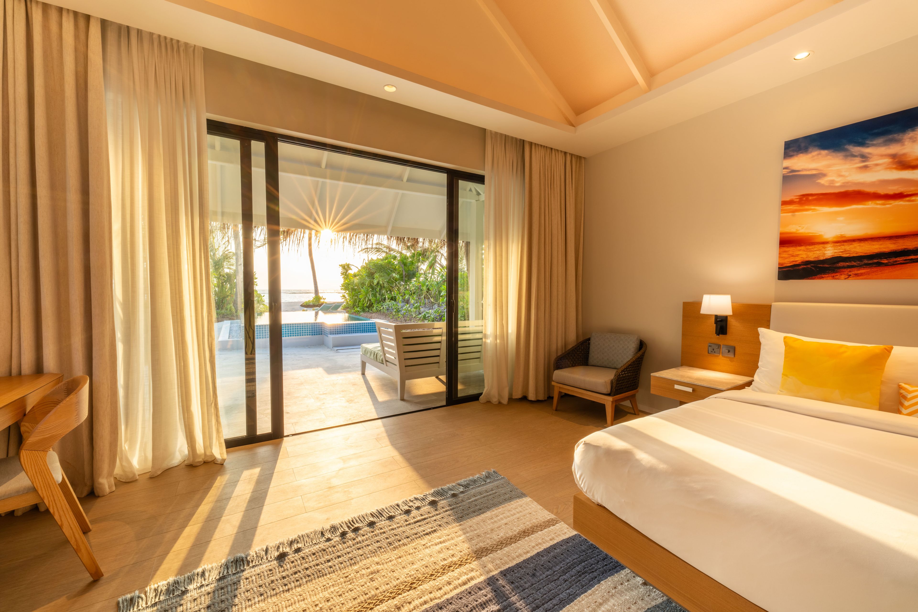 A bedroom with a bed, a chair, a desk, a nightstand, and a view of a pool and greenery.