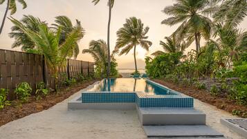 A swimming pool with tiled steps, surrounded by palm trees and a sandy area.