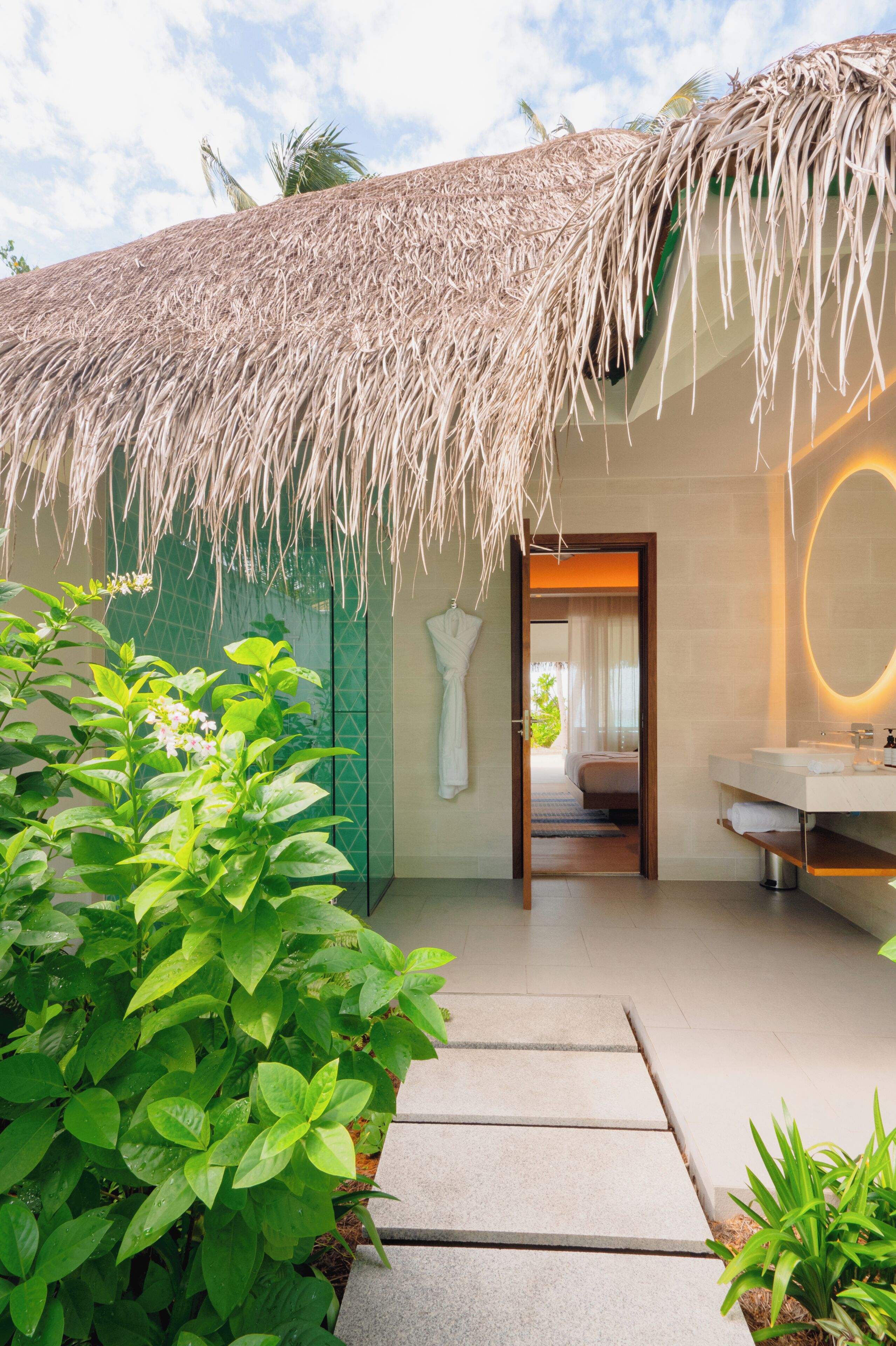 A modern hotel room with a thatched roof, a private bathroom, and a view of the beach.