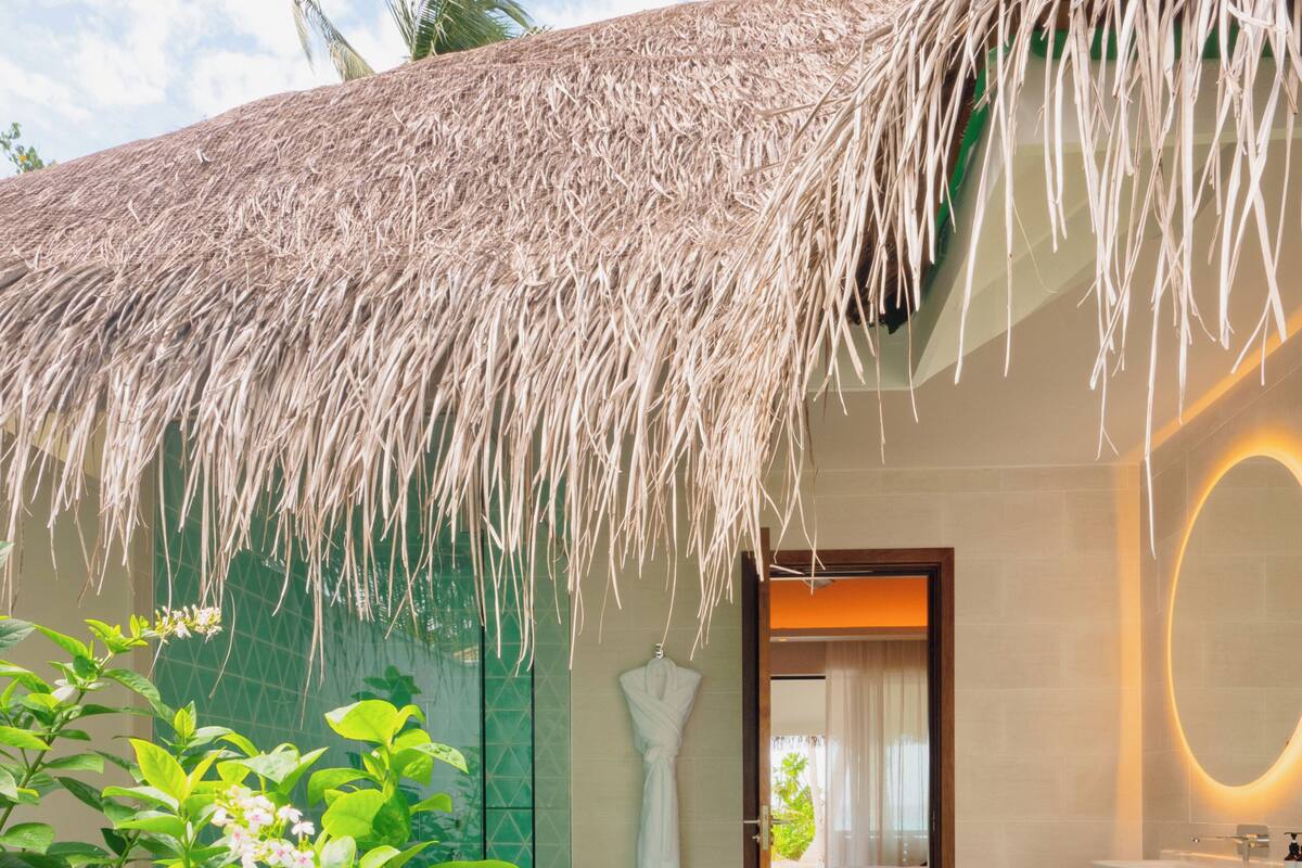 A modern hotel room with a thatched roof, a private bathroom, and a view of the beach.
