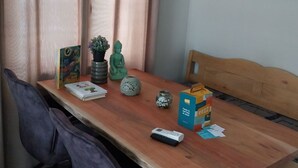 Een eethoek met een houten tafel, twee stoelen, een bankje, een kleine potplant, een decoratieve vaas, een boek, een afstandsbediening en een vruchtensapje.