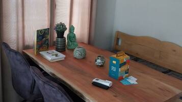 Een eethoek met een houten tafel, twee stoelen, een bankje, een kleine potplant, een decoratieve vaas, een boek, een afstandsbediening en een vruchtensapje.