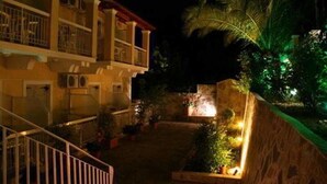 Ein Hotel mit Balkon, Treppe und beleuchtetem Gartenbereich bei Nacht.