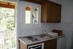 A kitchen with a window, white tiled backsplash, wooden cabinets, a sink, and a small appliance. - Marina Apartments & Studios (Corfu)