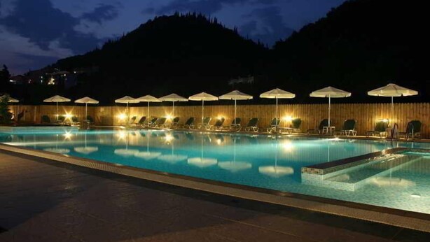 Ein Schwimmbecken mit Liegestühlen und Sonnenschirmen, umgeben von einem Holzzaun und einem Blick auf die Berge.