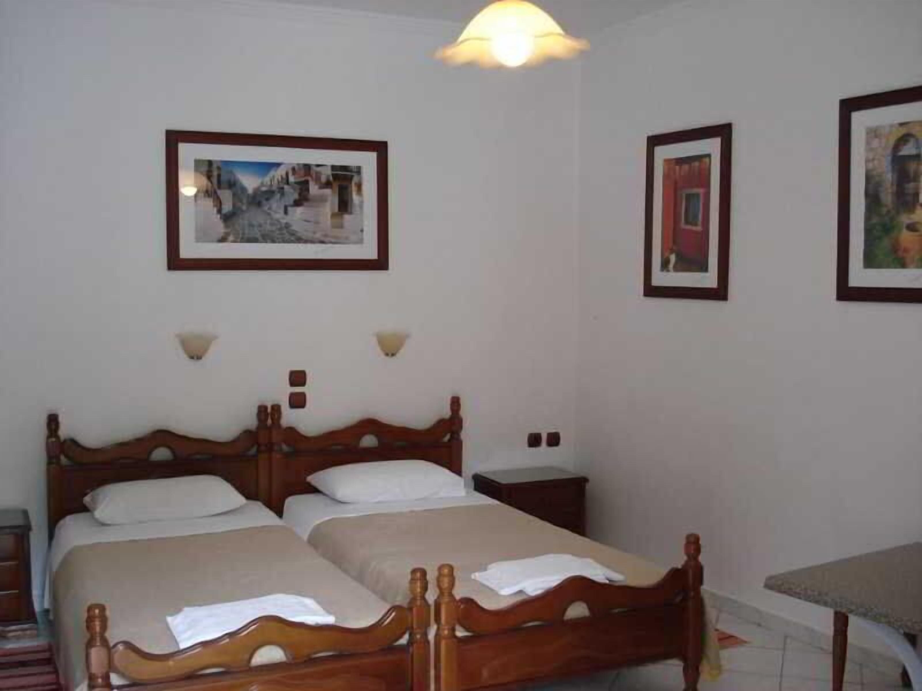 A bedroom with two wooden beds, a bedside table, a lamp, and framed pictures on the wall.