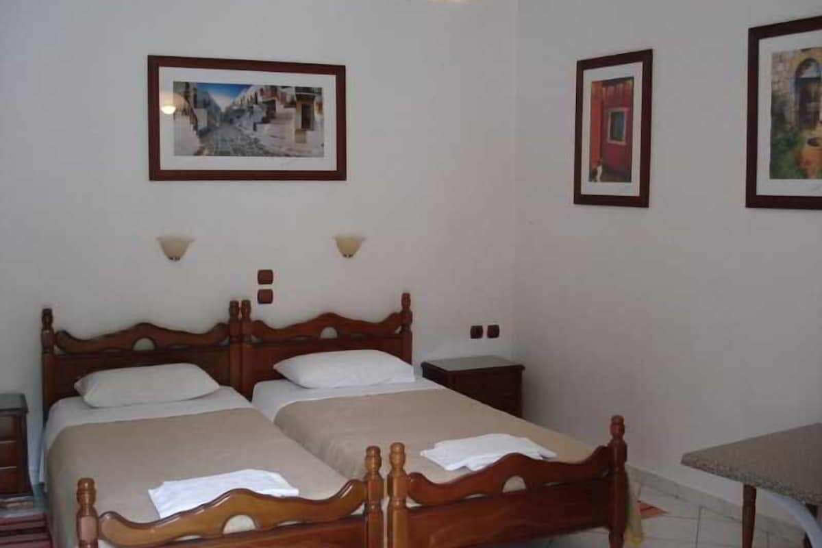 Una habitación con dos camas de madera, una mesita pequeña y lámparas fijadas a la pared.