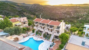 Un hotel moderno con piscina, varios balcones y vistas a las colinas circundantes.
