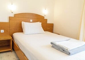 A neatly made bed with a wooden headboard, a bedside table, and two wall-mounted light fixtures. - Orestis (Chania)