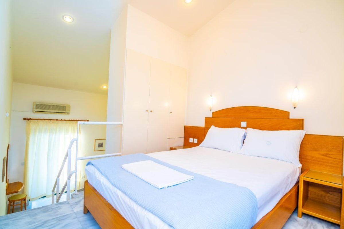 A hotel room with a large bed, bedside tables, a wooden headboard, and a window with curtains.