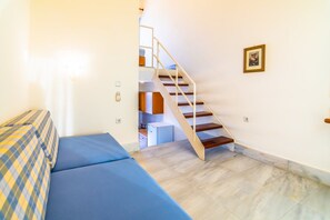 A room with a blue sofa, a staircase, and a small kitchen area. - Orestis (Chania)