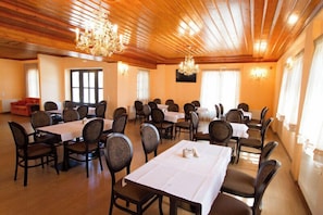 Une salle de conférence dotée de plusieurs tables et chaises, d’un plafond en bois et de lustres.