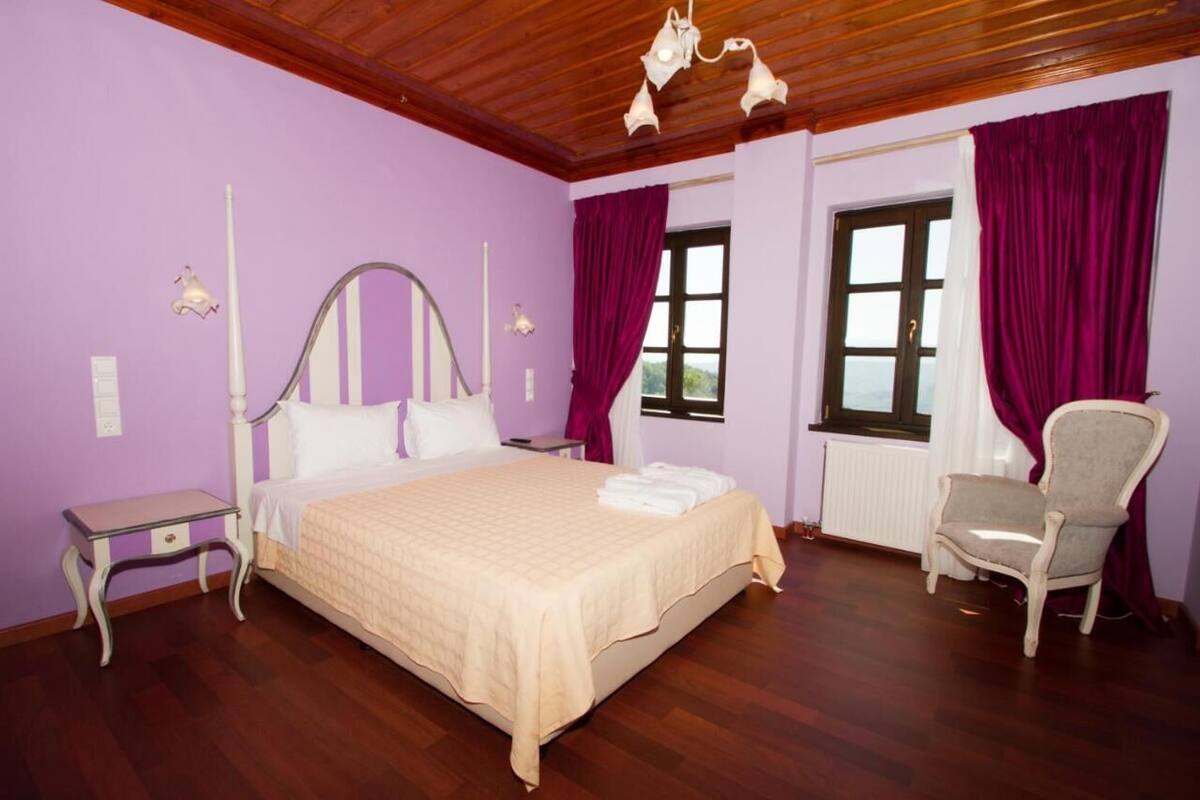 Un dormitorio con cama, mesita de noche, una silla y una ventana con cortinas.