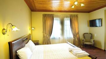 A hotel room with a wooden ceiling, a bed with white linens, a chair, a television, and curtains.
