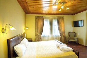 A hotel room with a wooden ceiling, a bed with white linens, a chair, a television, and curtains. - Monodendri (Zagori)