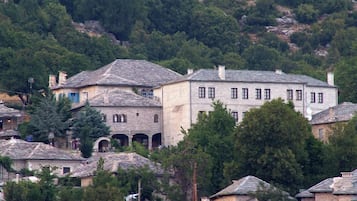 A stone building with multiple windows and a flat roof, surrounded by trees and other buildings.
