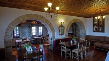 A dining area with stone arches, wooden furniture, and a chandelier.