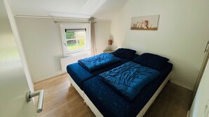 Een slaapkamer met twee bedden, een raam, een radiator en een schilderij aan de muur.