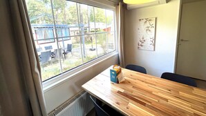 Een kamer met een groot raam, een houten tafel, een stoel, een hanglamp en een radiator.