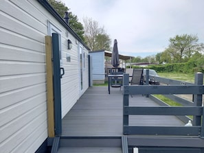 Ein überdachter Außenbereich mit Tisch und Stühlen, einer Holzterrasse und einem begrenzten Eingang.
