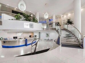 A modern hotel lobby with a reception desk, a staircase, and potted plants. - Mantra Sirocco Mooloolaba (Sunshine Coast)