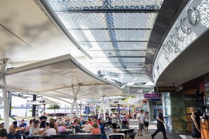 An outdoor dining area with tables and umbrellas, a reception sign, and a storefront with a sign that reads "Sugar Spice." - Mantra Sirocco Mooloolaba (Sunshine Coast)