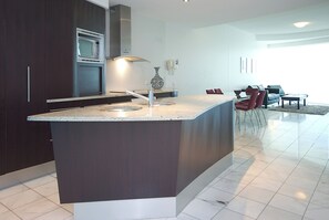 A modern kitchen with a central island, dark cabinetry, and a built-in microwave. - Mantra Sirocco Mooloolaba (Sunshine Coast)
