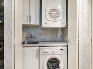 A compact laundry room with a built-in washer and dryer, a sink, and a ventilation unit above the dryer. - Mantra Sirocco Mooloolaba (Sunshine Coast)