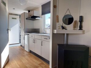 Eine moderne Küche mit Herd, Spüle und Schränken. Ein Fenster mit Jalousien, ein Spiegel an der Wand und ein schwarzer Heizkörper sind vorhanden.
