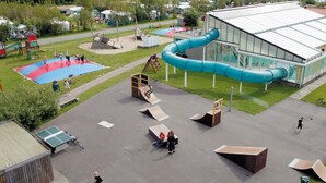 Een speeltuin met glijbanen en hellingbanen, een overdekt gebouw en een tennisbaan.