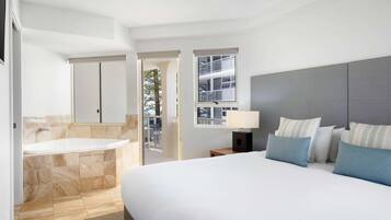 A modern hotel room with a large bed, a separate bathroom with a bathtub, and a balcony with a view of the building.