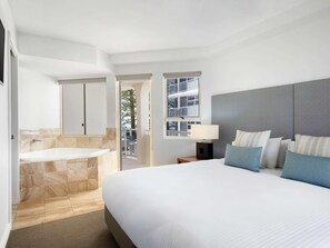 A modern hotel room with a large bed, a separate bathroom with a bathtub, and a balcony with a view of the building. - Mantra Zanzibar Mooloolaba (Sunshine Coast)