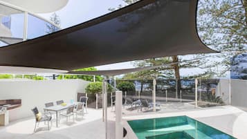 A modern outdoor pool area with a covered seating area and a view of the surrounding landscape.