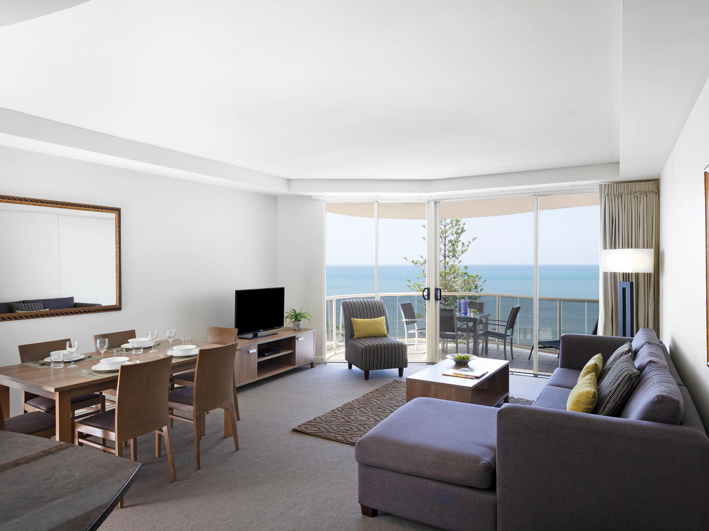 Ein modernes Wohnzimmer mit Essbereich, einem Flachbildfernseher und einem Balkon mit Meerblick.