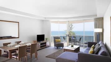 Ein modernes Wohnzimmer mit Essbereich, einem Flachbildfernseher und einem Balkon mit Meerblick.