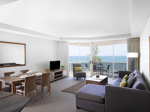 A modern living room with a dining area, a flat-screen TV, and a balcony with a view of the sea. - Mantra Zanzibar Mooloolaba (Sunshine Coast)