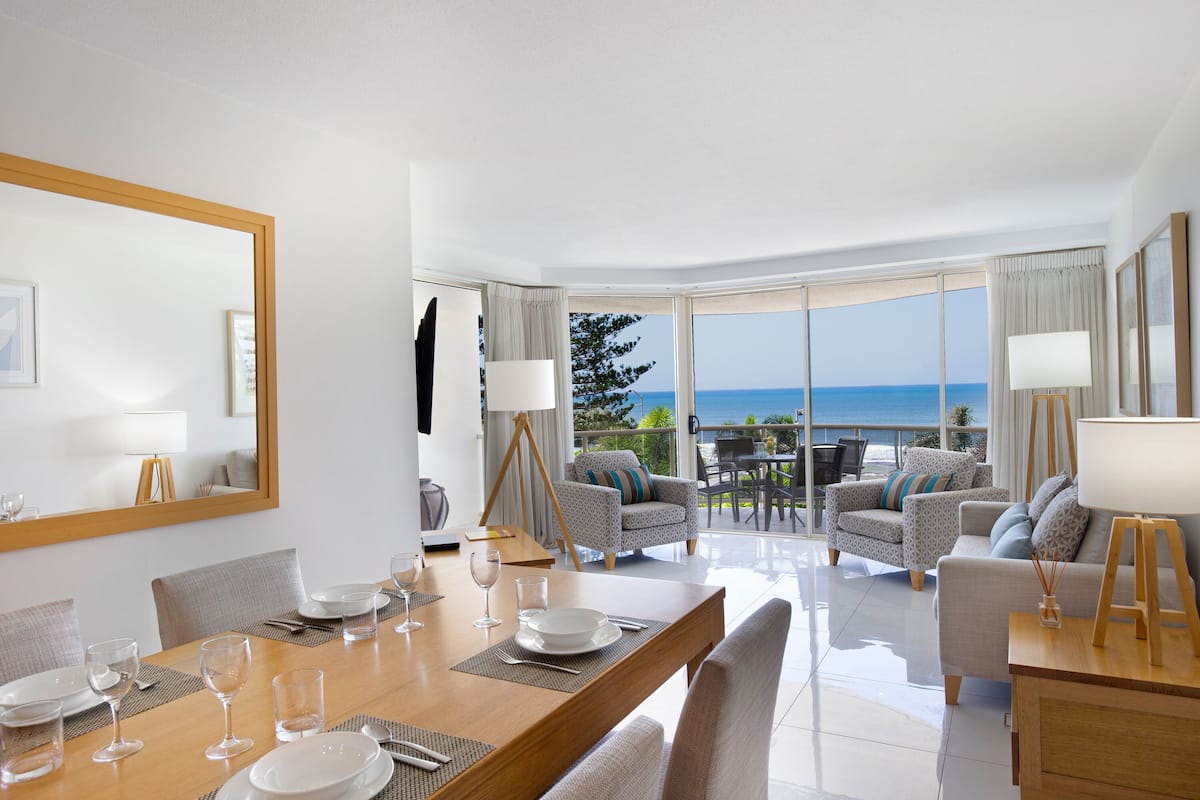 A modern hotel room with a dining area, a large mirror, and a view of the ocean.