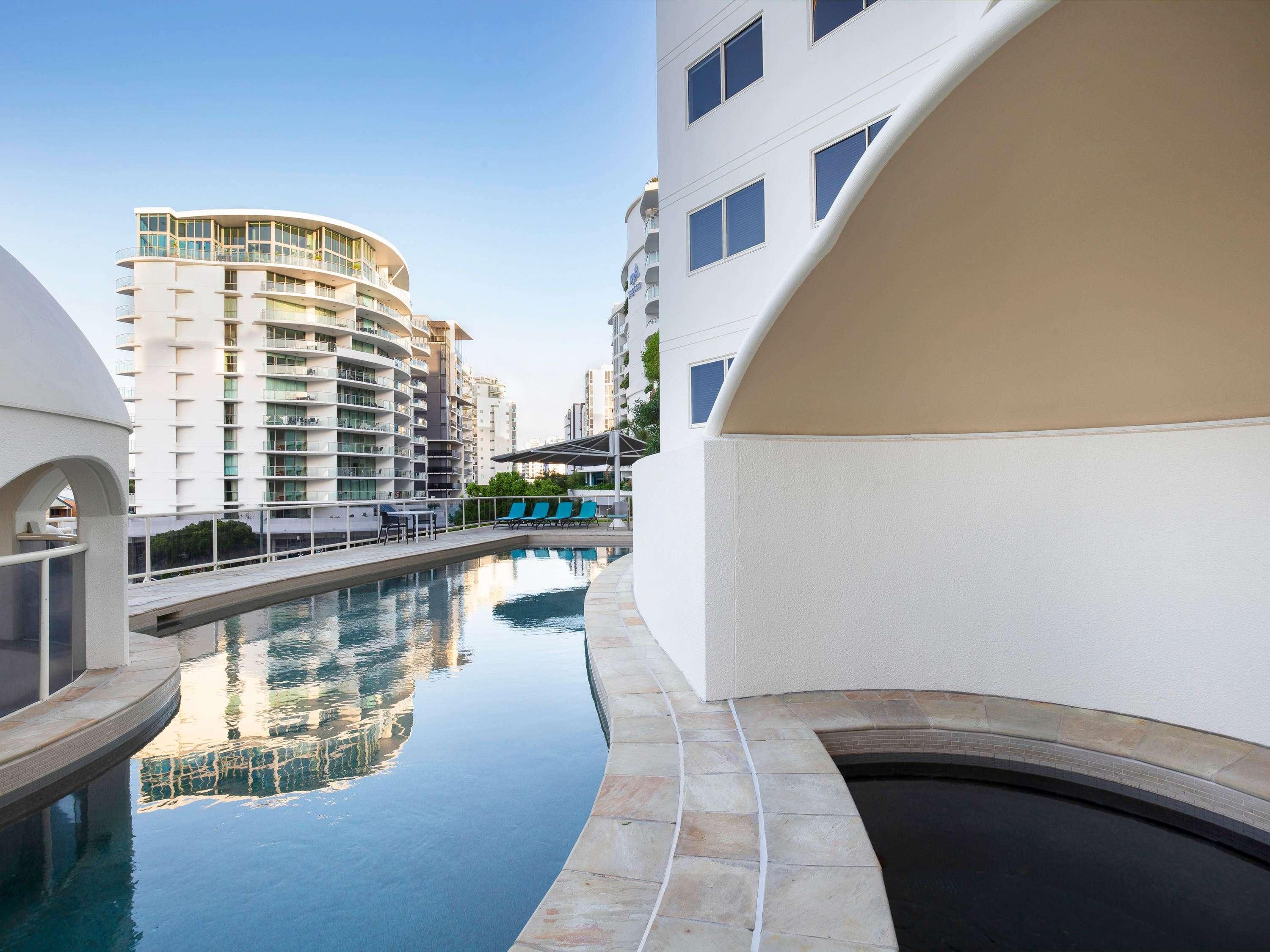 Un edificio moderno con piscina, varios balcones y cielo despejado.