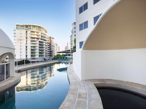 Um edifício moderno com piscina, várias varandas e céu claro.