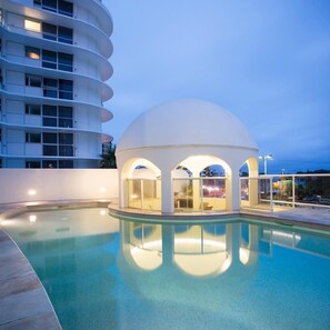 A swimming pool with a dome structure, a multi-story building in the background, and a clear sky. - Mantra Zanzibar Mooloolaba (Sunshine Coast)