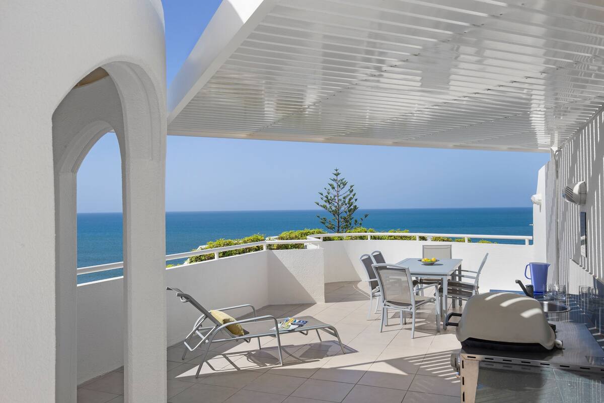 A terrace with a view of the sea, outdoor furniture, and a grill.