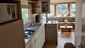 A compact kitchen with a stove, sink, and cabinets, a small dining area with a table and bench, and a window with a view of greenery. - RBR 434 - Beach Resort Kamperland by Interhome (Kamperland)