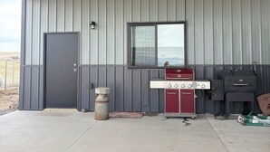 Et overdækket udendørs område med metalvæg, dør, vindue og grill.