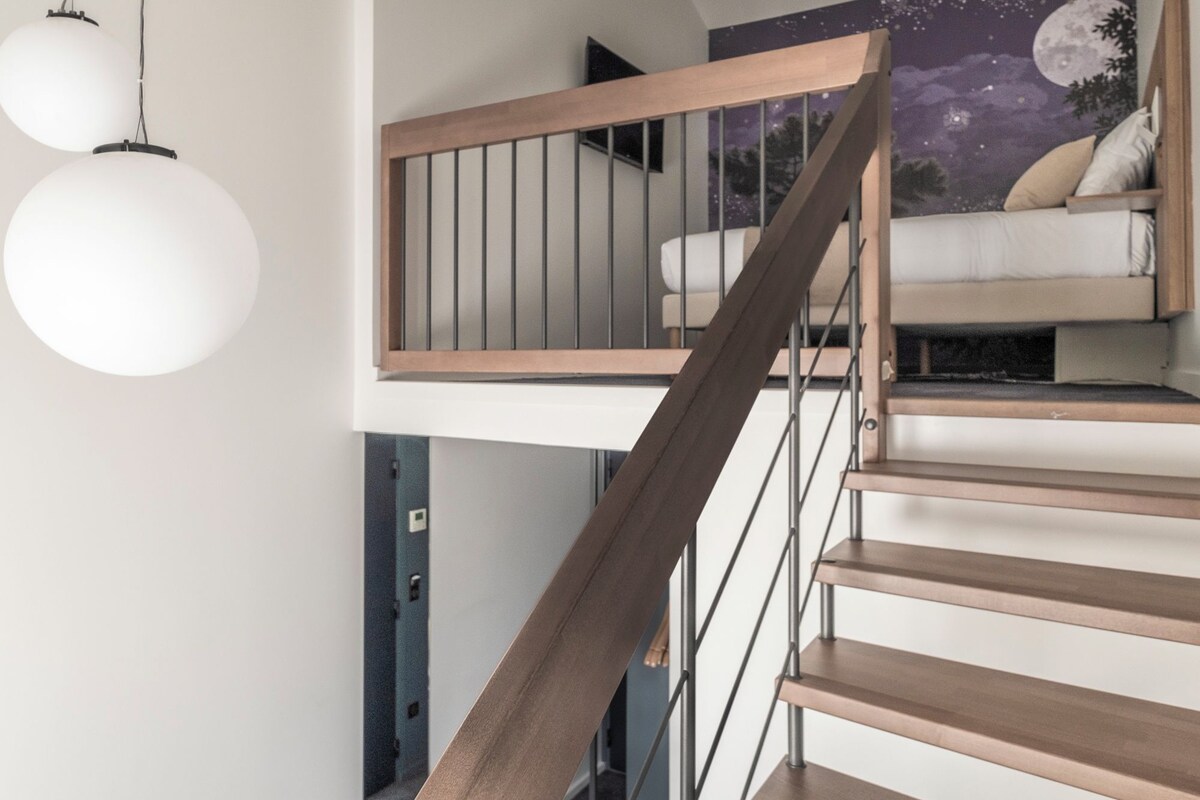 A modern staircase with wooden steps and metal railings, leading to a loft bedroom with a night sky mural.