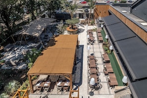 An outdoor dining area with wooden tables and chairs, a covered seating area, and a pool. - Hotel le Relais des Brasseurs (Aubagne)