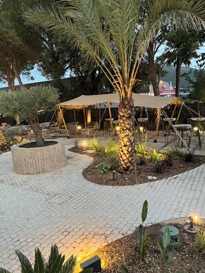 An outdoor seating area with tables and chairs, a palm tree, and a stone planter. - Hotel le Relais des Brasseurs (Aubagne)